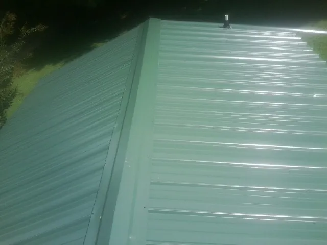 New green metal panels meeting at the ridge of a roof — Flat Roof Repair work by our crew in Gig Harbor