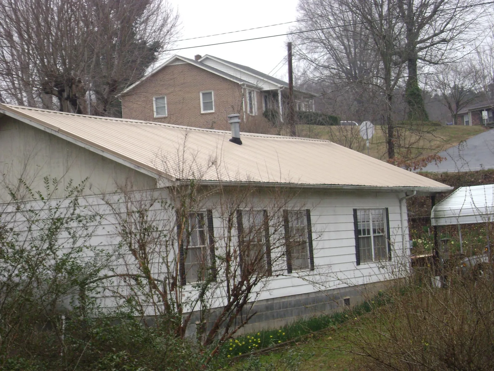 Tan metal roof on a white sided house set into a hillside — Commercial Roofing by Roofing Brothers in Gig Harbor